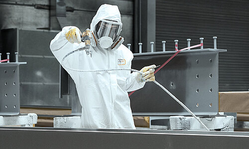 Fachkraft führt eine industrielle Nasslackbeschichtung in einer Beschichtungskabine aus.